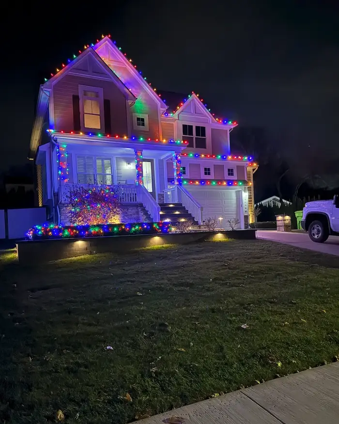 The same home at night, with multicolor lights along every roofline, the porch posts and the front garden.