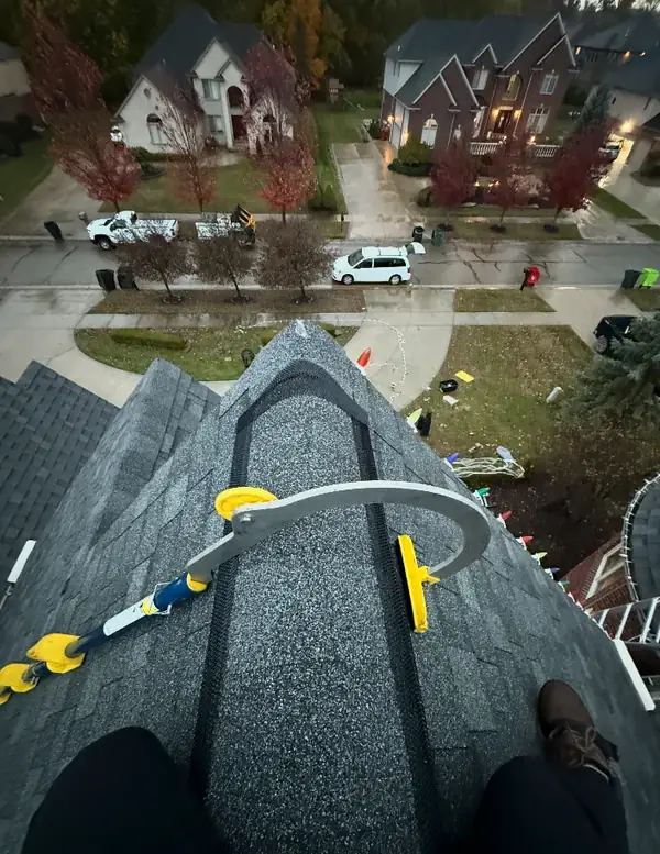 Looking down from a roof peak on a rainy evening, with a ladder hook on the ridge and lights going up.