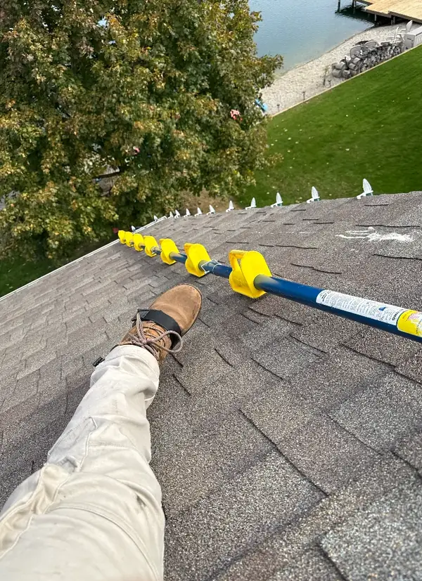 A crew member on a lakeside roof with a ladder stabilizer, next to a run of light clips.
